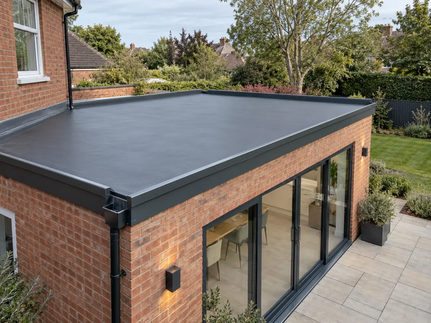 Single-ply flat roof on a brick house extension with grey edge trims, bi-fold doors and a patio